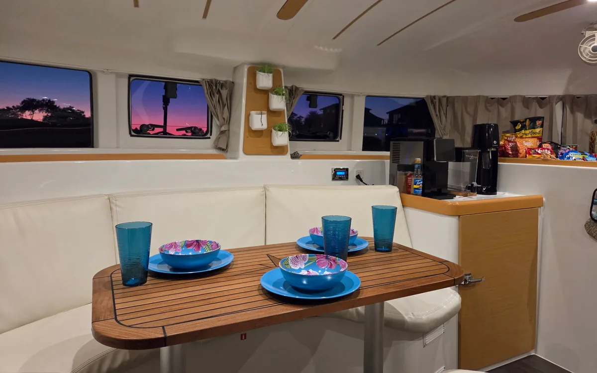 Majik’s salon set for a meal: teal cups and plates on the wood dining table, sunset in the windows